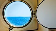Blick auf ein Meer durch ein Bullauge einer Schiffskabine. © picture alliance / Bildagentur-online/Tetra Images | Bildagentur-online/Tetra Images 