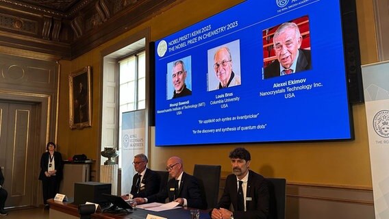 Während der Bekanntgabe des Nobelpreises für Chemie sind auf einem Bildschirm die Porträts der Wissenschaftler Moungi Bawendi (l-r), Louis Brus und Alexei Ekimov zu sehen. © dpa Foto: Steffen Trumpf