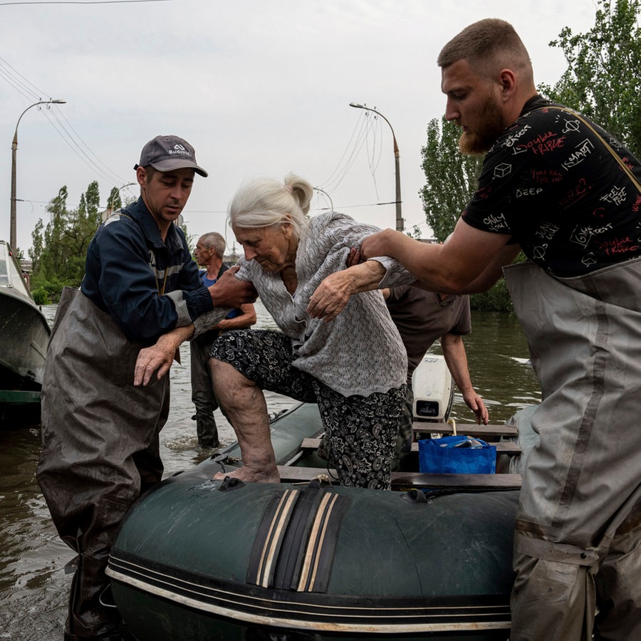 Rettungskräfte evakuieren eine ältere Frau aus einem überfluteten Viertel in der südukrainischen Stadt Cherson. © AP/dpa Foto: Evgeniy Maloletka