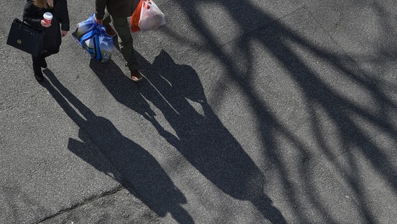 Zwei Personen mit langen Schatten, der auf eine Straße fällt, tragen ihren Einkauf. © picture alliance Marcus Brandt dpa Foto: Marcus Brandt
