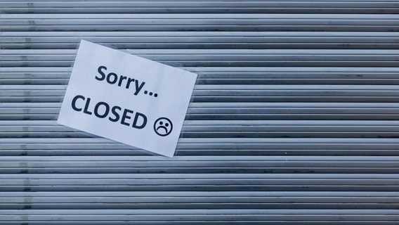 "Entschuldigung geschlossen" ist auf ein Stück Papier geschrieben, das an den Taschenläden eines geschlossenen Geschäfts klebt.  © Bild Allianz / dpa Foto: Rolf Vennenbernd