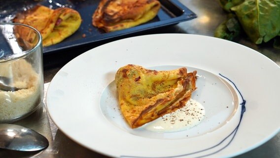 Crespelle mit Spinat, Schinken und Mozzarella und etwas Soße auf einem Teller angerichtet. © NDR Foto: Florian Kruck