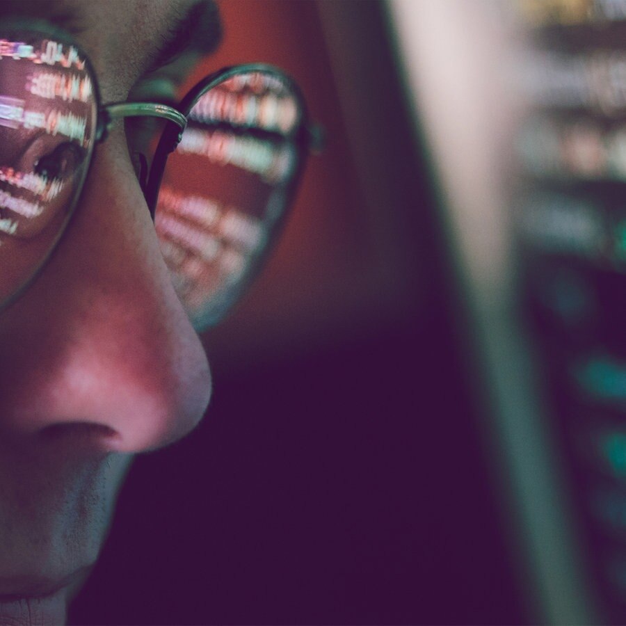 Ein Mann sitzt vor einem Bildschirm, in seiner Brille spiegeln sich die Zahlen und Zeichen die der Bildschirm abbildet. © photocase.de Foto: przemekklos