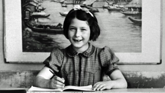 Irene Butter als kleines Mädchen an einem Schreibtisch, sie lächelt in die Kamera. © NDR 