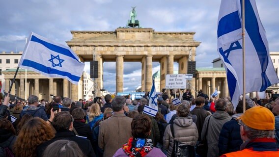 Teilnehmer der Kundgebung "Aufstehen gegen Terror, Hass und Antisemitismus · in Solidarität und Mitgefühl mit Israel"  schwenken israelische Flaggen vor dem Brandenburger Tor in Berlin. © dpa Foto: Monika Skolimowska