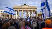 Teilnehmer der Kundgebung "Aufstehen gegen Terror, Hass und Antisemitismus · in Solidarität und Mitgefühl mit Israel"  schwenken israelische Flaggen vor dem Brandenburger Tor in Berlin. © dpa Foto: Monika Skolimowska