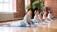 Drei Frauen und zwei Mann in der Cobra-Pose während einer Yogastunde © Syda Productions 