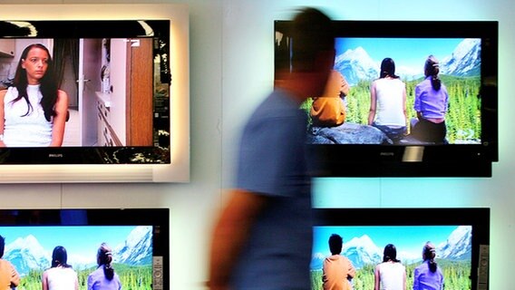 Ein Mann geht an einer Reihe von mehreren Flachbildfernsehern vorüber. © dpa Foto: Arno Burgi