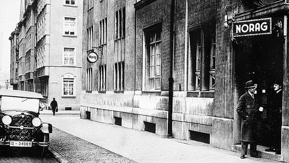 Straßenszene aus den 1930er-Jahre, zwei Männer stehen im Eingang eines Gebäudes der NORAG. © NDR 