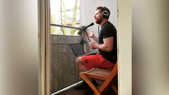 Andreas Kuhlage sitzt während er moderiert in Shorts auf seinem Balkon, da er sich wegen der Corona-Krise im Homeoffice befindet. Andreas Kuhlage sitzt während er moderiert in Shorts auf seinem Balkon, da er sich wegen der Corona-Krise im Homeoffice befindet. © N-JOY