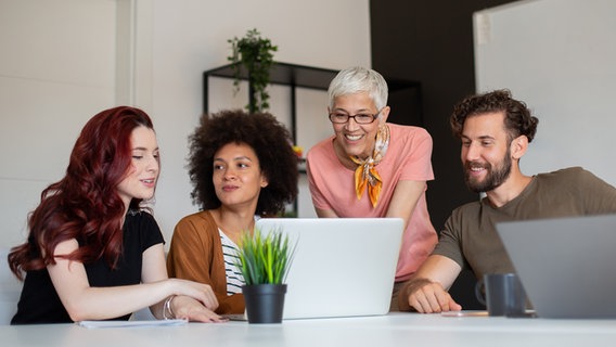 Eine Gruppe von vier Menschen bespricht sich und arbeitet mit zwei Laptops. Zwei junge Frauen, eine ältere und ein junger Mann. © - Foto: -