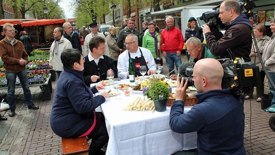 Rainer Sass am Tisch mit Wochenmarkthändlern © dmfilm und tv produktion GmbH & Co. KG 