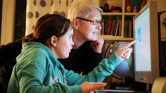 Ein Mädchen und eine ältere Frau schauen gemeinsam auf einen Computer-Bildschirm. © imago/Petra Schneider 