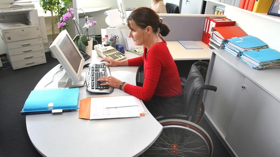 Rollstuhlfahrerin an ihrem Schreibtisch im Büro © imago/INSADCO 