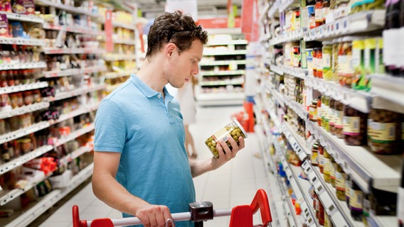Ein Mann steht in einem Supermarkt zwischen den Regalen und schaut sich ein Produkt an. © Fotolia Foto: anyaberkut