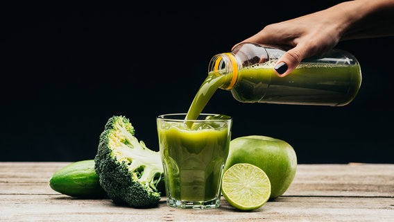 Brokkoli, Gurke, Apfel und Limette liegen um ein Glas, das mit einem grünem Smoothie gefüllt wird. © panthermedia Foto: VadimVasenin
