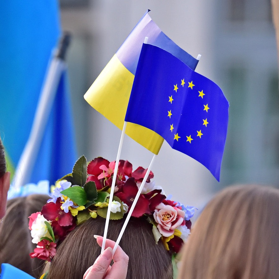 Eine ukrainische und eine EU-Papierflagge wehen nebeneinander auf einer Kundgebung für Solidarität mit der Ukraine an der Hauptwache in Frankfurt am Main im Juni 2022. © picture alliance / Daniel Kubirski | Daniel Kubirski 