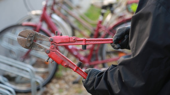 Ein Mann mit schwarzen Handschuhen hält einen Bolzenschneider, im Hintergrund sieht man Fahrräder © IMAGO Foto: SKATA