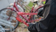Ein Mann mit schwarzen Handschuhen hält einen Bolzenschneider, im Hintergrund sieht man Fahrräder © IMAGO Foto: SKATA