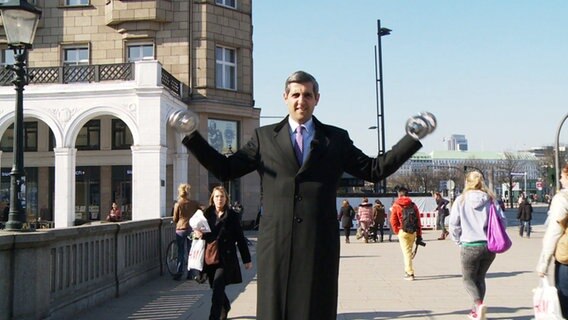 Michel Abdollahi steht mit Hanteln in den Händen auf einem Podest in der Hamburger Innenstadt.  
