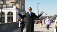 Michel Abdollahi steht mit Hanteln in den Händen auf einem Podest in der Hamburger Innenstadt.  