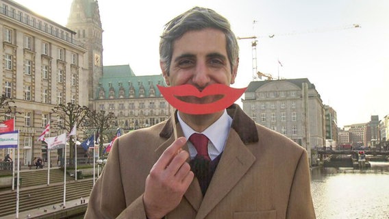 Michel Abdollahi hält sich einen roten lächelnden Papiermund vors Gesicht.  