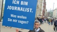 Michel Abdollahi mit einem Schild in der Hand: Ich bin Journalist. Was wollen Sie mir sagen? © NDR 