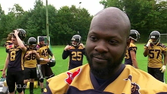 Ein Footballspieler, im Hintergrund ist sein Team zu sehen.  