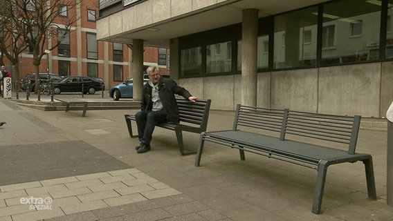 Ein Mann sitzt auf einer von zwei verschiedenen Bänken.  