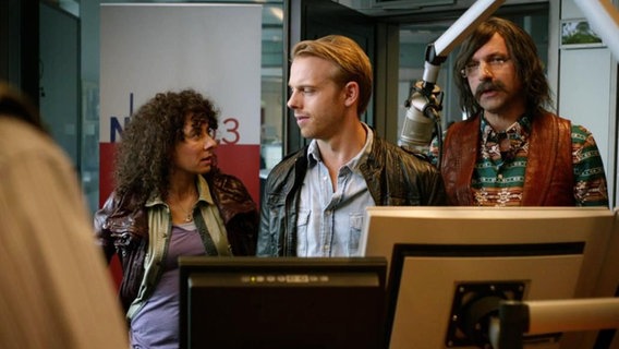 Drei Personen stehen in einem Radio- Studio.  