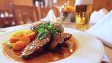 Rinderschmorbraten (Böfflamott) mit Soße, Knödeln und Karotten auf einem Teller serviert.  