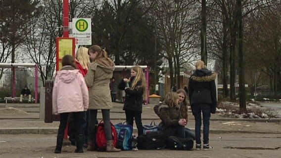 Schüler warten an einer Bushaltestelle auf den Bus.  