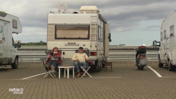 Ein altes Ehepaar sitzt auf Plastikgartenmöbeln auf einem Campingplatz aus Beton.  