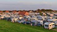 Viele Wohnwagen auf Neuharlingersiels Campingplatz hinter dem Deich im warmen Licht des Abends. © picture alliance / Michael Narten Foto: Michael Narten
