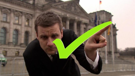 Ein junger Mann zeichne einen Haken auf die Mattscheibe. Im Hintergrund sieht man den deutschen Bundestag.  