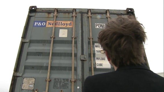 Ein Mann steht vor einem Container.  