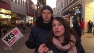 Zwei junge Menschen in einer Fußgängerzone, der eine hält ein Plakat mit der Aufschrift "WSD, Wir sind dagegen", die andere Person zeigt mit dem Finger in die Kamera.  