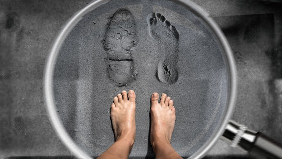 Ein Mann steht barfuß im Sand, vor ihm sind zwei Fußabdrücke, einer von einem Stiefel, einer von einem nacktem Fuß. © photocase.de, panthermedia Foto: Tom Baur