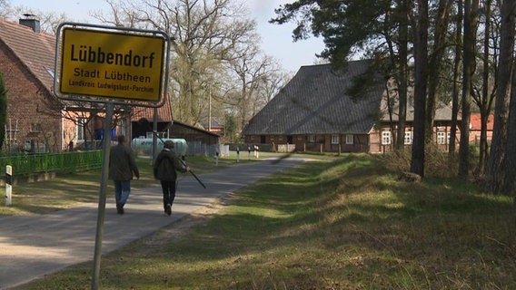 Das Kamerateam läuft am Ortsschild von Lübbendorf vorbei auf ein Haus zu.  
