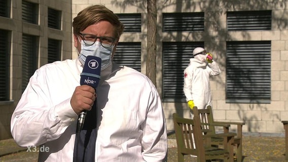 Ein NDR-Reporter mit Mundschutz spricht ins Mikro.  