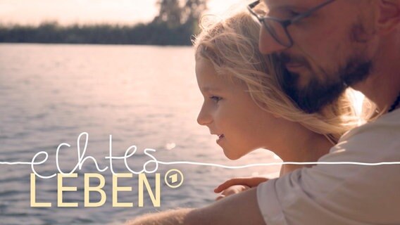 Ein Vater blickt mit seiner Tochter bei untergehender Sonne auf einen See. © ARD 