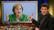 Der Extra3-Moderator Christian Ehring. Im Hintergrund Bundeskanzlerin Merkel.  