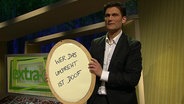 Moderator Christian Ehring mit einem Schild mit der Aufschrift, wer das umdreht ist doof, in der Hand.  