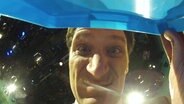 Der Moderator Christian Ehring schaut in eine Box mit versteckter Kamera.  