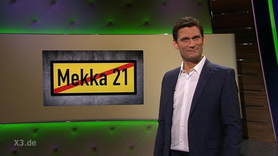 Christian Ehring neben einem Schild mit der Aufschrift "Mekka 21".  
