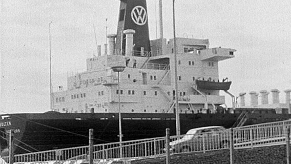 Archiv-Bild in Schwarz-Weiß eines Schiffs mit dem VW-Logo auf dem Schornstein. Im Vordergrund fährt ein VW-Auto eine Rampe herab. © Screenshot 