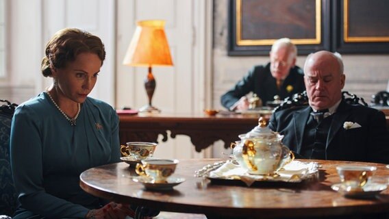 Szenenbild aus der norwegischen Serie "Atlantic Crossing": Eine Frau und ein Mann sitzen an einem Kaffeetisch. Im Hintergrund sitzt ein Mann am Schreibtisch. © NDR/Julie Vrabelová 