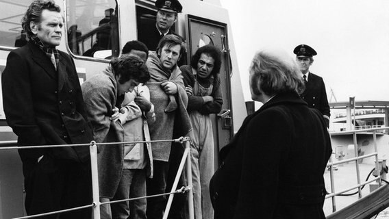 Peter Jörgensen (Christoph Quest, vorne rechts) wartet darauf, dass Kapitän Meider (Hans Heine, links) und seine geretteten Besatzungsmitglieder von Bord gehen. © NDR/Lilo-Foto 