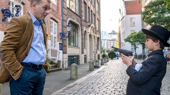 Der kleine Florian (Kian Lars Parsiani-Schmidt, r.) aus dem Kinderheim St. Gertrud bedroht am helllichten Tag als Mafiosi verkleidet den Anwalt Bender (Hans Christoph Michel, l.) mit einer Waffe. Der kleine Florian (Kian Lars Parsiani-Schmidt, r.) aus dem Kinderheim St. Gertrud bedroht am helllichten Tag als Mafiosi verkleidet den Anwalt Bender (Hans Christoph Michel, l.) mit einer Waffe. © ARD/Georges Pauly