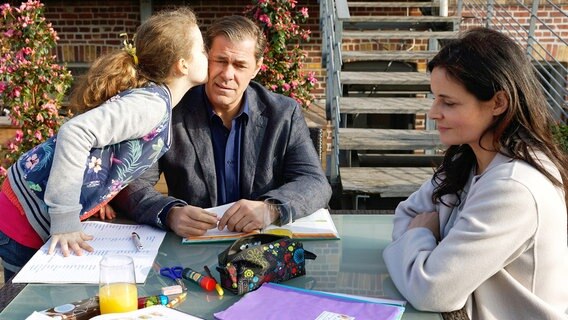Christoph (Sven Martinek, M.) hat Pflegetochter Luisa (Deborah Mary Schneidermann, l.) bei den Hausaufgaben geholfen - sie bedankt sich zum Abschied mit einem Kuss. Susanne (Elisabeth Lanz, r.) genießt die häusliche Szene. Christoph (Sven Martinek, M.) hat Pflegetochter Luisa (Deborah Mary Schneidermann, l.) bei den Hausaufgaben geholfen - sie bedankt sich zum Abschied mit einem Kuss. Susanne (Elisabeth Lanz, r.) genießt die häusliche Szene. © NDR/ARD/Ulf Boettcher